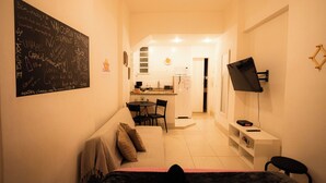 Un espace de vie compact comprenant un coin cuisine, un coin repas et un espace détente avec un canapé et des fauteuils.