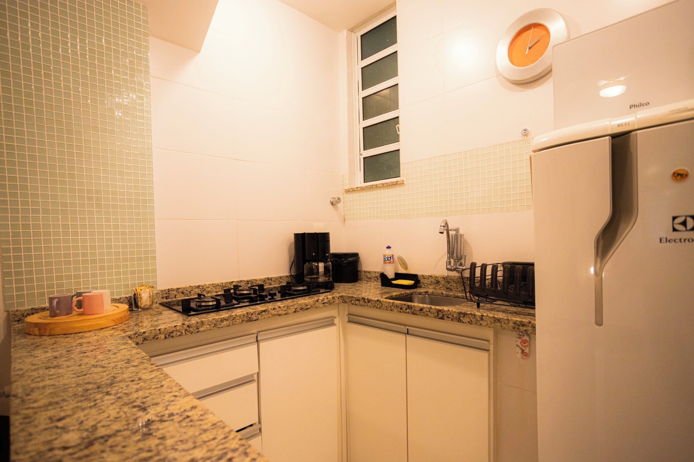 A kitchen with white cabinets, a stainless steel refrigerator, a coffee maker, and a window with blinds.