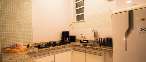 A kitchen with white cabinets, a stainless steel refrigerator, a coffee maker, and a window with blinds.