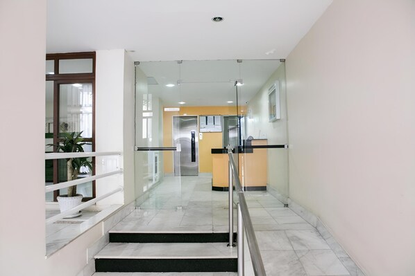 A modern interior with a glass-walled reception area, a staircase with metal railings, and a potted plant.