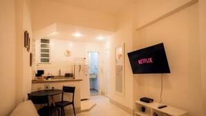 Un espace de vie compact comprenant un coin cuisine, un coin repas et un téléviseur fixé au mur.
