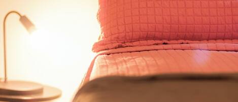 Una cama con cubrecama acolchado rosa y negro, una lámpara de noche y una ventana con cortinas.