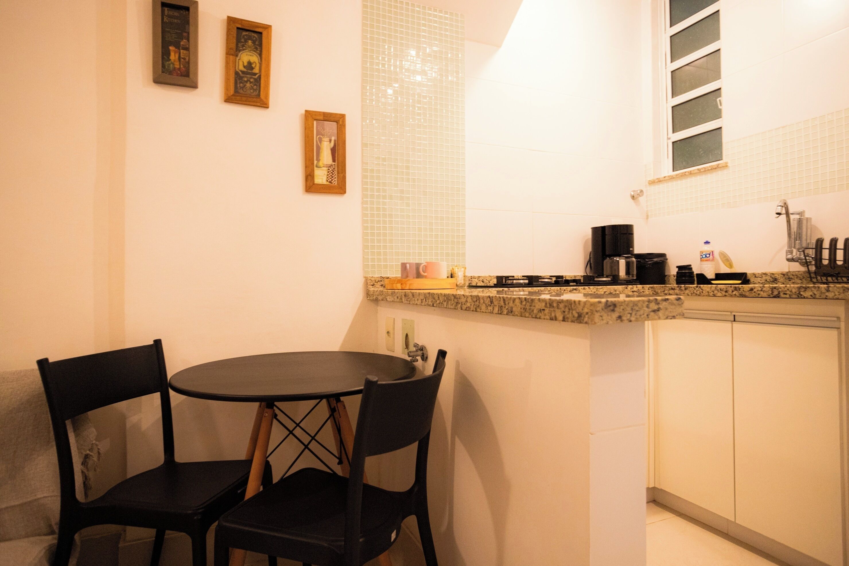 A small kitchen with a round table and two chairs, a coffee maker, and a window above the sink.