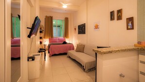 Une chambre d’hôtel de taille réduite, comprenant un lit, un canapé, une petite table et un ventilateur de plafond.