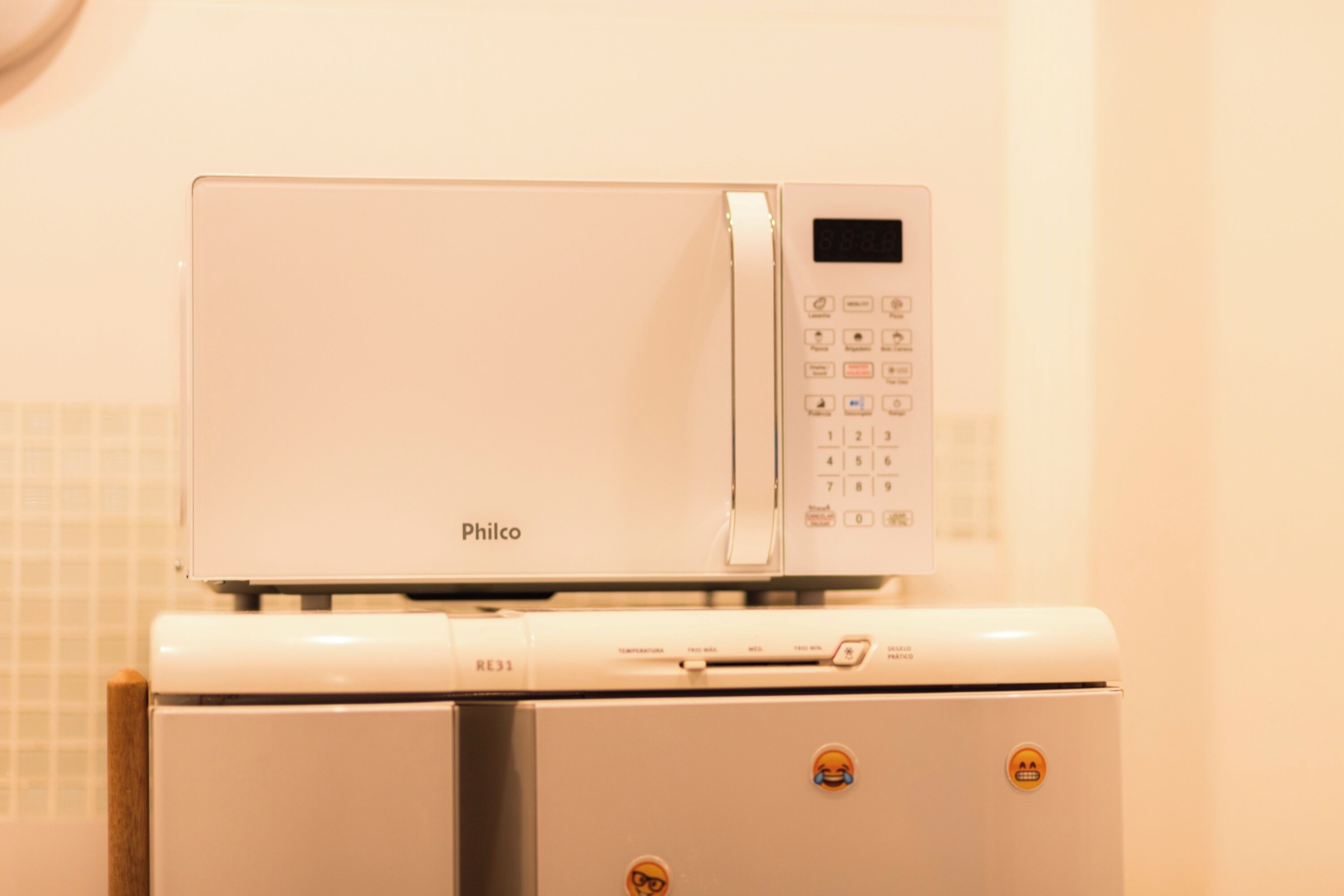 A white microwave oven with a digital display and control panel, placed on a white appliance with a control panel and a small display.