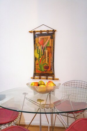 Uma sala de jantar com uma mesa de vidro, cadeiras vermelhas e uma obra de arte pendurada na parede.