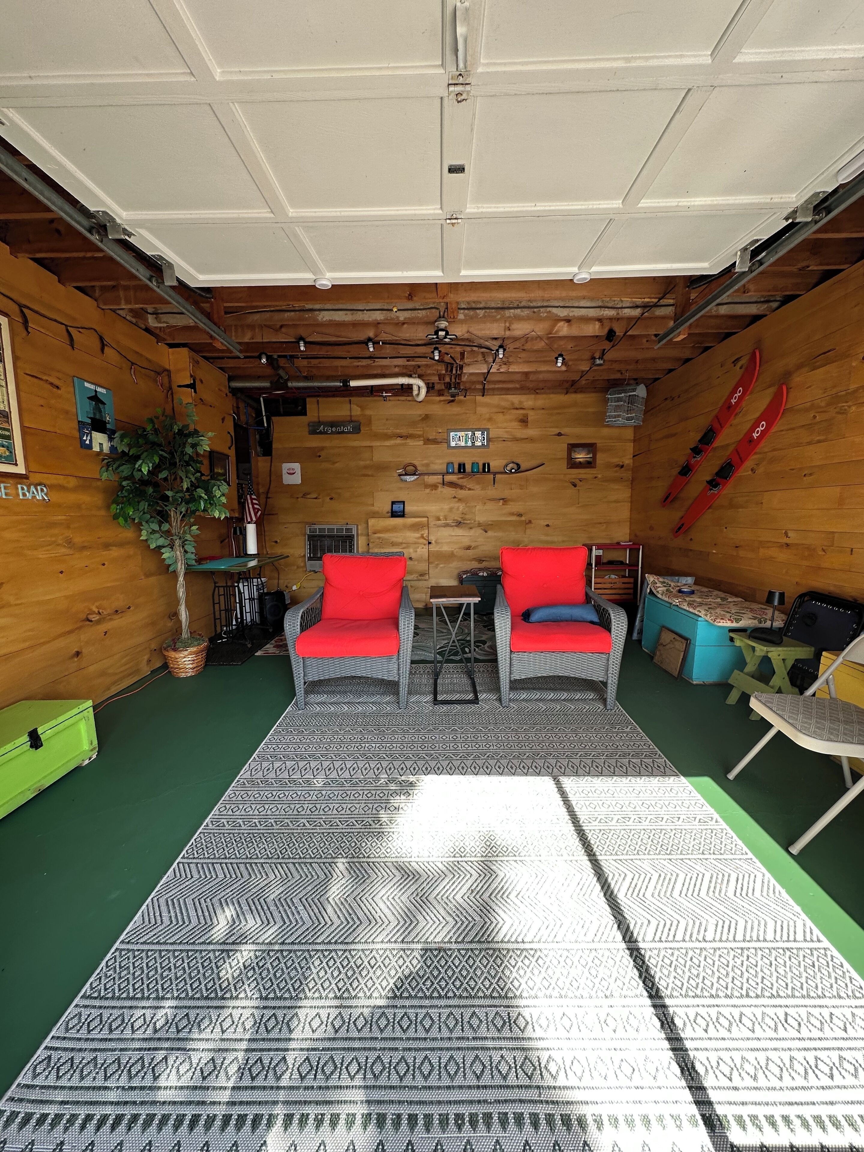 A cozy room with a wooden ceiling, two red chairs, a patterned rug, and skis on the wall.