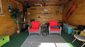 A cozy room with a wooden ceiling, two red chairs, a patterned rug, and skis on the wall.