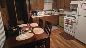 Une cuisine avec des meubles de rangement en bois, un réfrigérateur blanc, une cuisinière et une table à manger avec des sets de table.