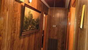 Un couloir aux murs en bois, avec un tableau encadré, un thermostat et une grille d’aération.