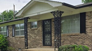 Une maison à deux étages avec une façade en briques, un porche à l’avant orné de colonnes décoratives et un petit jardin devant.