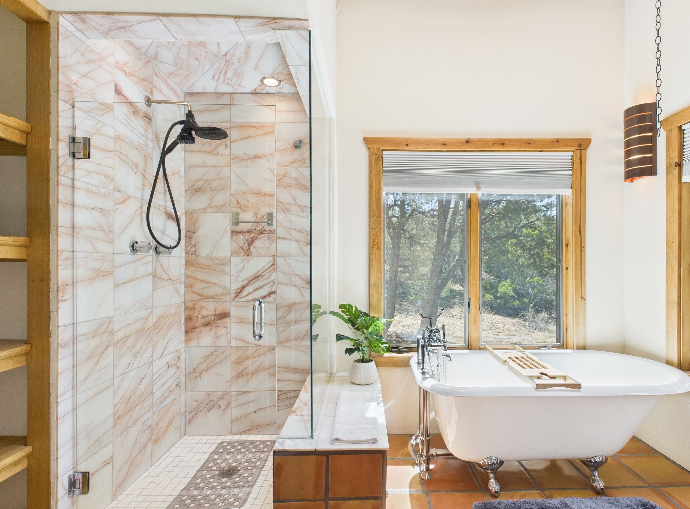 Un bagno con doccia, vasca e una finestra vista alberi.