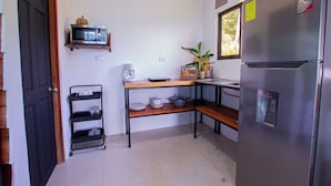 A compact kitchen with a refrigerator, microwave, and a small shelf with dishes.