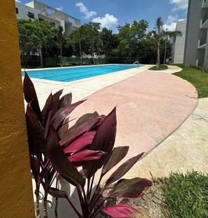 Area piscina con vialetto in cemento, circondata da verde e edifici moderni.