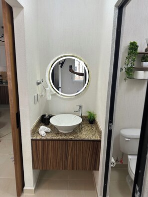 Un bagno con uno specchio rotondo, un lavabo bianco e un mobile vanitario in legno.