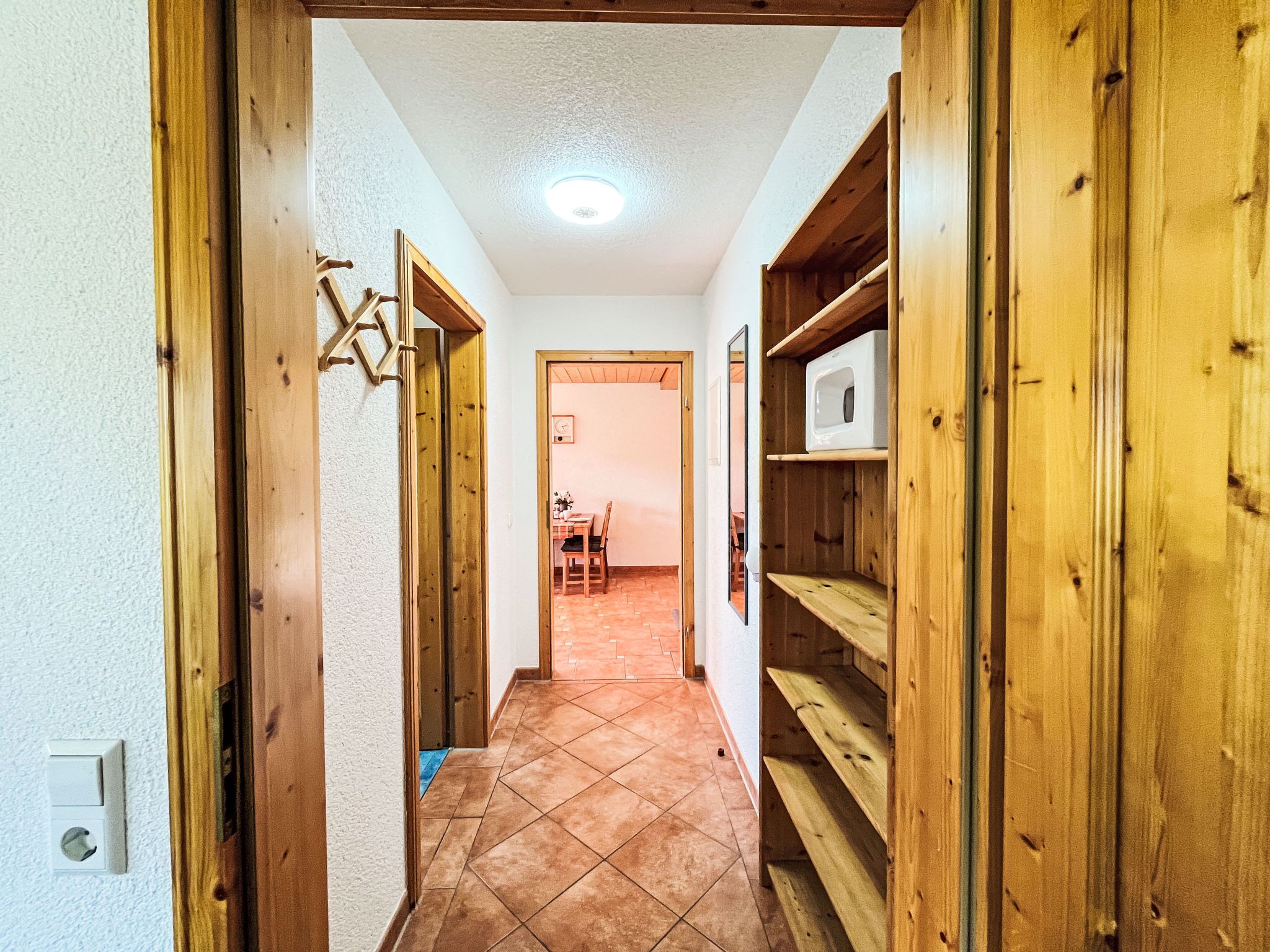 Un couloir avec des portes et des étagères en bois, qui mène à une salle à manger.