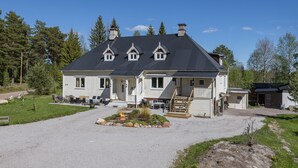 Una casa de dos pisos con techo oscuro, fachada blanca y un porche con mobiliario exterior.