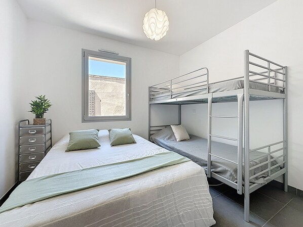 Una habitación tipo dormitorio con literas, una ventana con vistas, un aparador y una lámpara colgante.