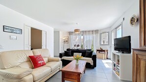 A modern living room with a beige sofa, a black sofa, a wooden coffee table, and a television on a wooden cabinet.