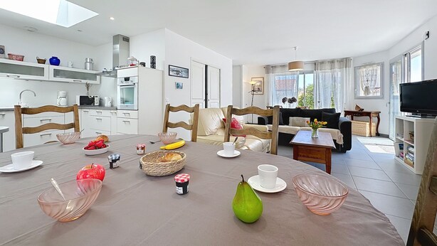 A modern kitchen with white cabinets, a dining area with a round table, and a living room with a sofa and TV.