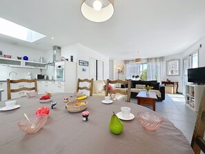 Une cuisine moderne avec des meubles blancs, un coin repas doté d’une table ronde et un salon avec un canapé et une télévision.
