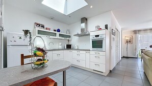 A modern kitchen with white cabinets, a skylight, a dining table with a fruit basket, and a sofa in the adjacent living area.
