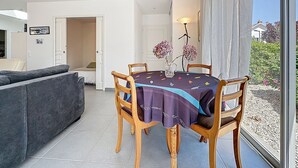 A dining area with a table set for four, surrounded by wooden chairs, a cushioned sofa, and a large window offering a view of the garden.