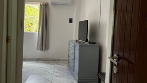 Ein Zimmer mit Marmorboden, einem grauen Schrank mit einem Flachbildfernseher, einem Fenster mit Vorhängen und einer Klimaanlage an der Wand.