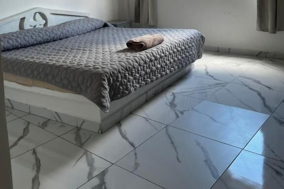 Een slaapkamer met een bed, een plafondventilator, een raam met gordijnen en een betegelde vloer.