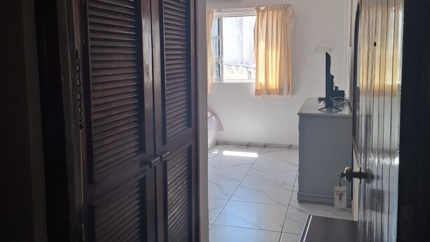 Ein Zimmer mit Fliesenboden, Schreibtisch, Stuhl, Kleiderschrank und einem fensterbepflegten Fenster.