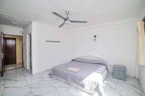 Une chambre à coucher avec un lit, un ventilateur de plafond, une table de chevet, une porte et un interrupteur sur le mur.