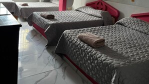 Ein Hotelzimmer mit drei Betten, einem Deckenventilator, einem Fenster mit Vorhängen und einer Wandleuchte.