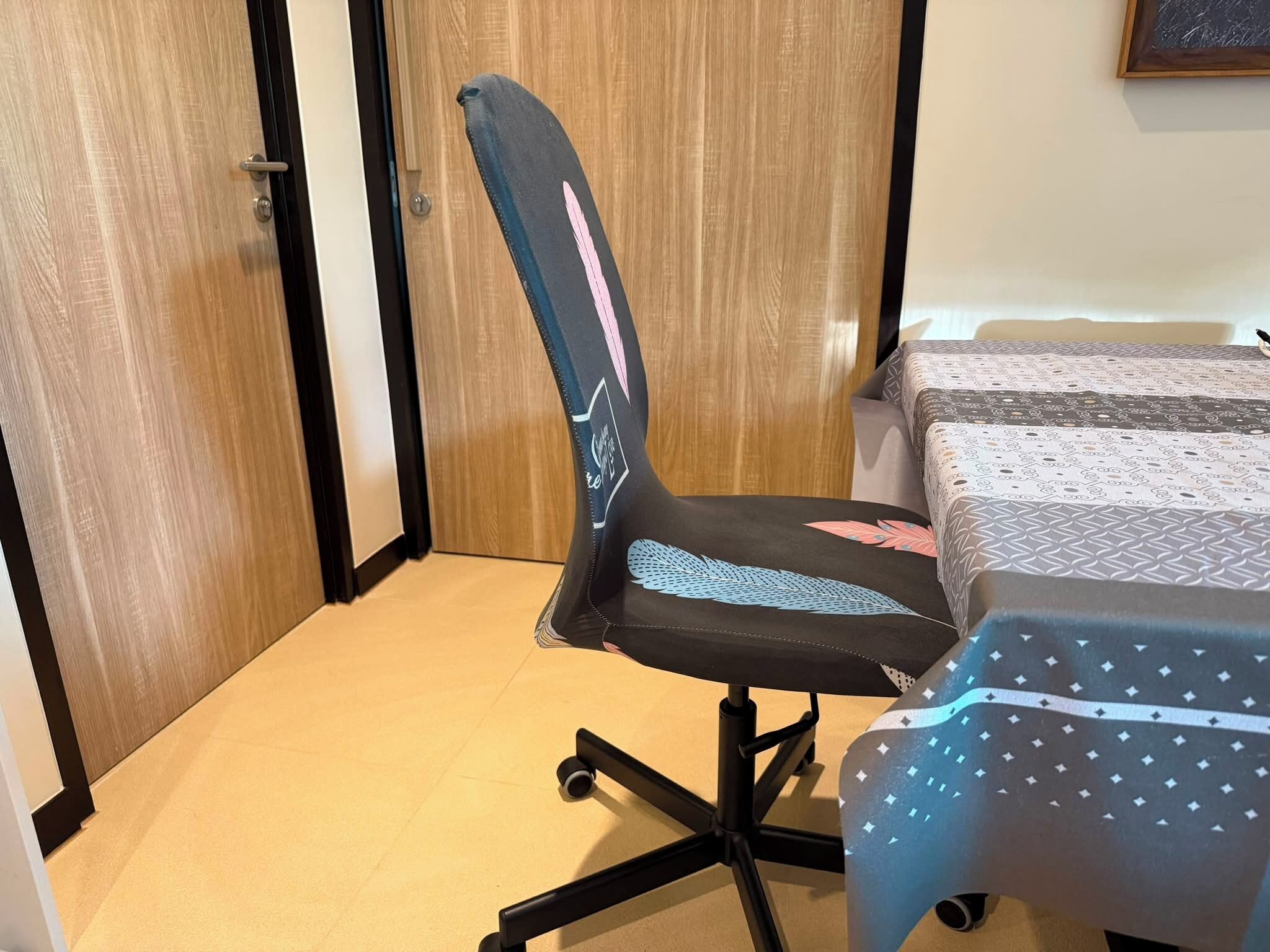 Een kamer met een houten deur, een bureau met een tafelkleed met dessin en een stoel met bladmotief.