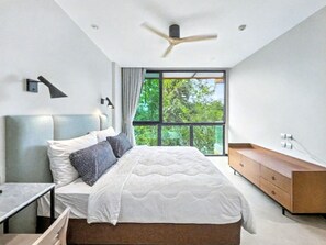 Une chambre moderne comprenant un lit, une table de chevet, une commode, un ventilateur de plafond, une fenêtre et une commode intégrée en bois.