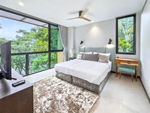 Ein Schlafzimmer mit großem Fenster, einem Bett, einem Schreibtisch und einem Deckenventilator.