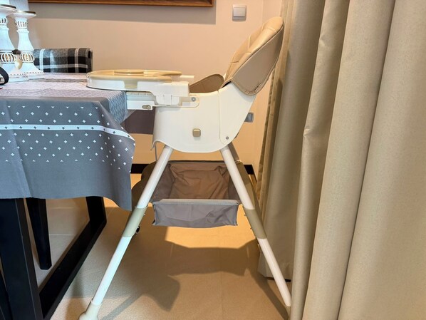A room with a dining table, a baby high chair, and a curtain.