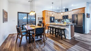 A modern kitchen with wooden cabinets, a central island, bar stools, and a dining area with a table and chairs. - Stylish Santa Fe Escape New Home by Lake, River & Casinos! (Bullhead City)