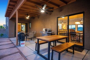 Une terrasse extérieure équipée d’un barbecue, de tables et de chaises, d’un ventilateur de plafond et offrant une vue sur l’intérieur grâce à une porte vitrée.