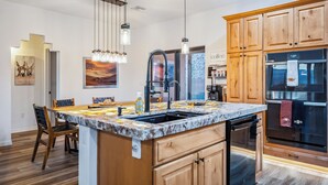 A modern kitchen with wooden cabinets, a marble countertop, a built-in sink, and stainless steel appliances. - Stylish Santa Fe Escape New Home by Lake, River & Casinos! (Bullhead City)