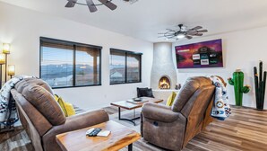 A modern living room with leather sofas, a fireplace, a flat-screen TV, and a ceiling fan. - Stylish Santa Fe Escape New Home by Lake, River & Casinos! (Bullhead City)