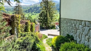 Il s’agit d’une propriété résidentielle dotée d’un mur en pierre, d’un chemin menant à une maison, et offrant une vue sur une vallée verdoyante, avec des arbres et des collines en arrière-plan.