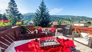 Une terrasse extérieure avec une table dressée pour deux personnes, un barbecue et une vue sur les montagnes.
