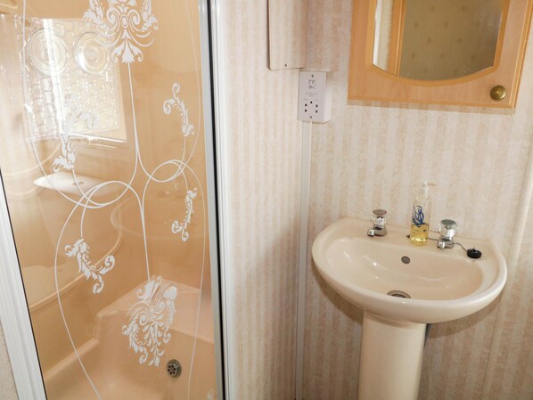 A bathroom with a glass shower door, a sink with a soap dispenser, and a mirror above the sink.