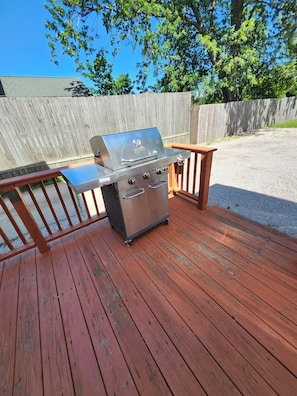 A portable stainless steel grill with a control panel and a side table on a wooden deck.