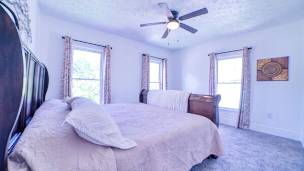 A bedroom with a bed, a ceiling fan, and two windows with curtains.