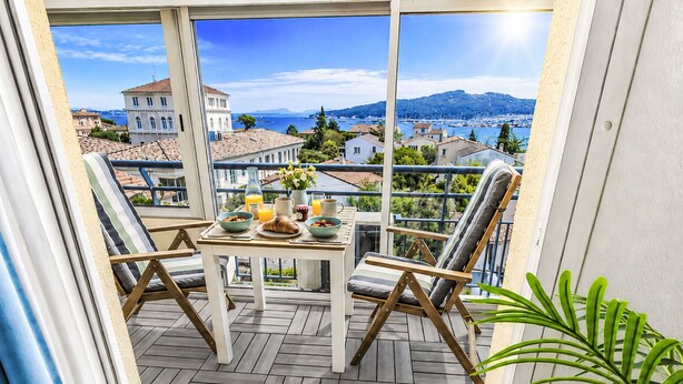 Ein Balkon mit Frühstückstisch, zwei Stühlen und Blick auf eine Küstenstadt.