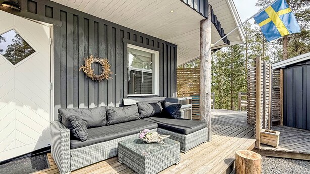 Een moderne buitenruimte met een grijze modulaire bank, een klein tafeltje met bloemen en een houten terras.