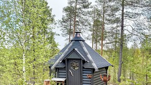 Een klein huisje met een donker dak en een houten deur, omringd door een dicht bos.