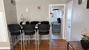 Un comedor con mesa y sillas, una cocina al fondo y una planta en maceta sobre una mesita.