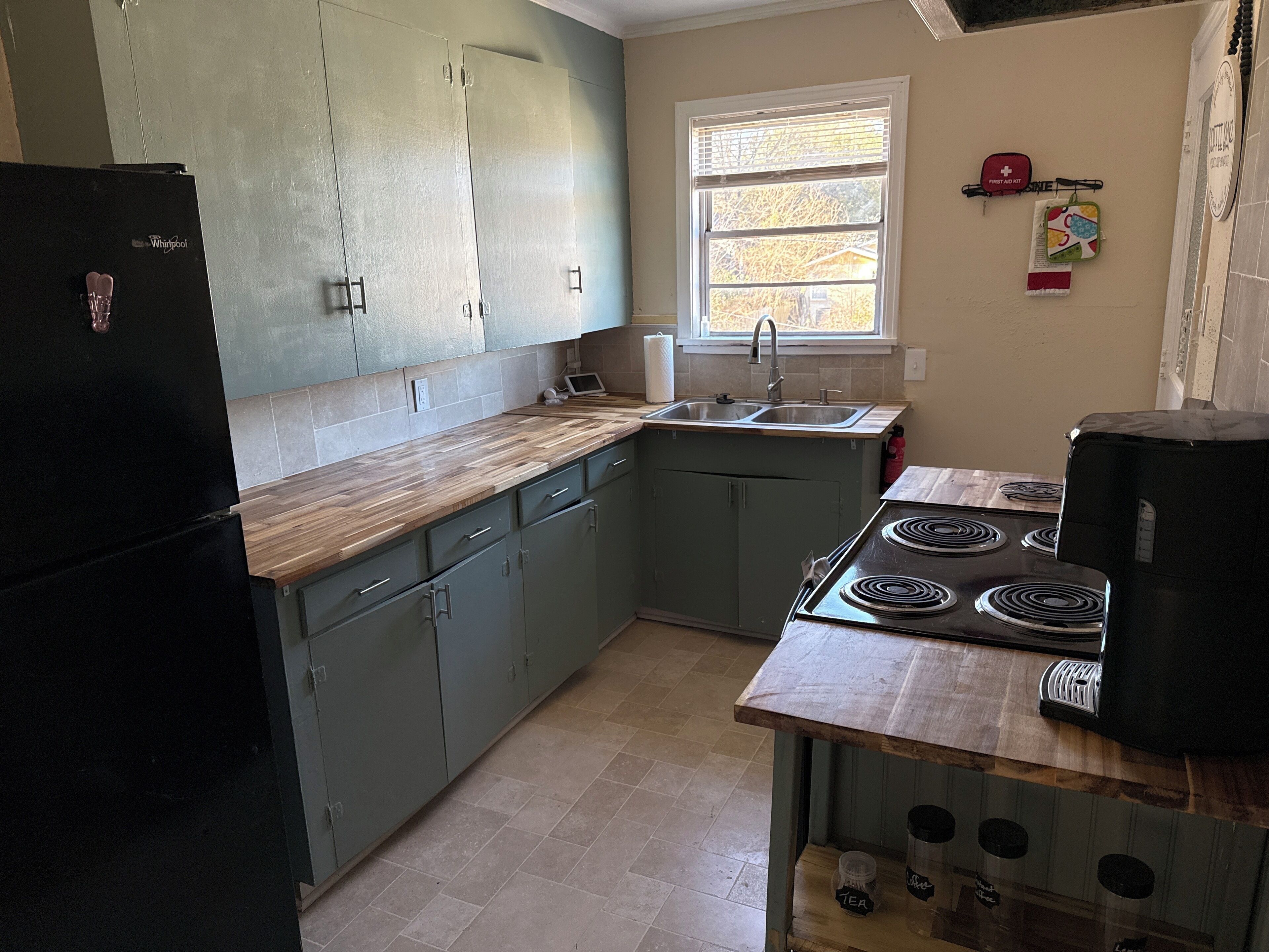 A kitchen with green cabinets, a black refrigerator, a sink, and a stove.